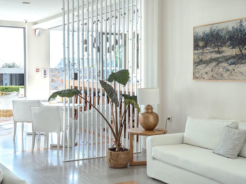 Zona living luminosa con divano bianco, piante e zona pranzo con vista sull'acqua.