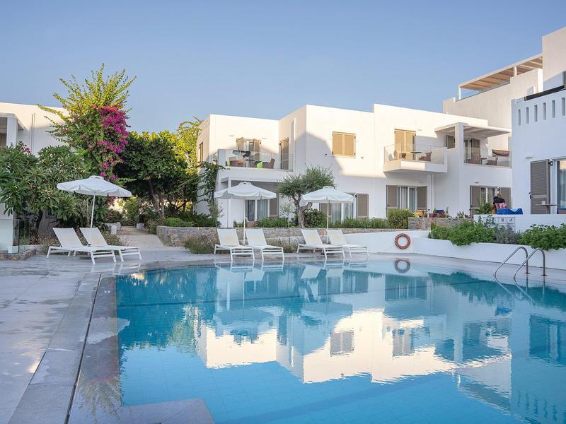 Piscina moderna dell'hotel con lettini e ombrelloni bianchi di fronte a edifici imbiancati.