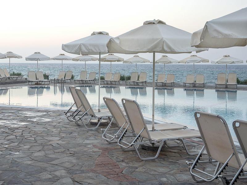 Sdraio e ombrelloni vuoti accanto alla piscina con vista sul mare calmo.