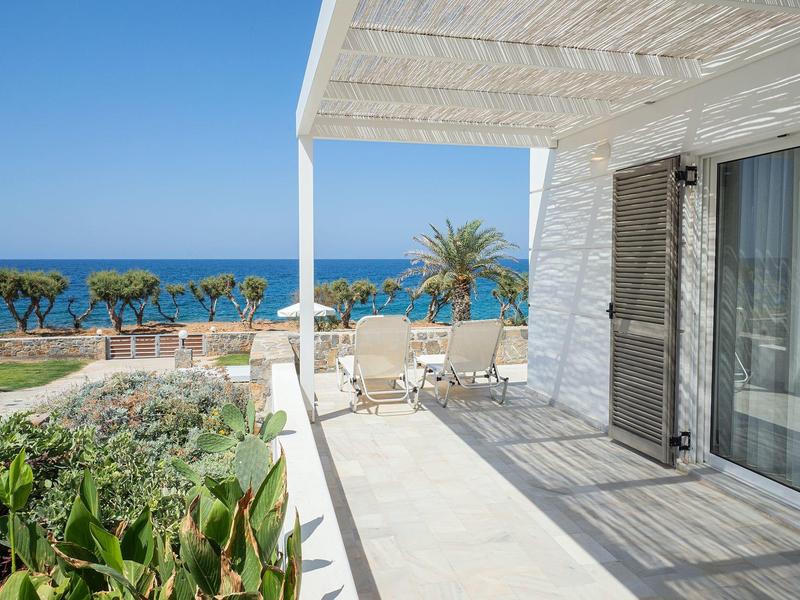 Terrazza piastrellata luminosa con vista sul mare e giardino sotto un cielo blu.