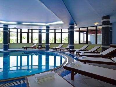 Indoor pool with lounge chairs and large windows letting in daylight.