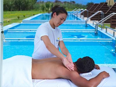 Person receiving a back massage beside an outdoor pool with loungers in the background.