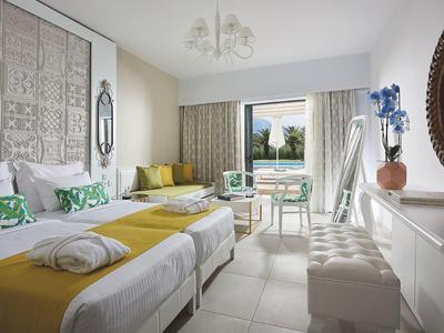 Helles Hotelzimmer mit zwei Betten, gelben Decken, Sitzbereich und großem Fenster mit Blick.