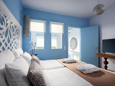 Hellblaue Schlafzimmer mit Doppelbett, weißen Kissen, Holzkommode und Fenster mit Vorhängen.