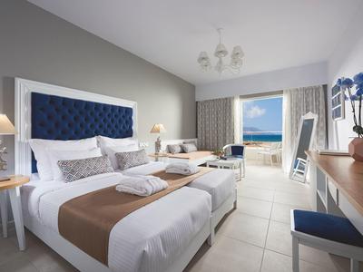Modernes Hotelzimmer mit Doppelbett, blauen Akzenten, Sitzbereich und Meerblick durch großes Fenster.