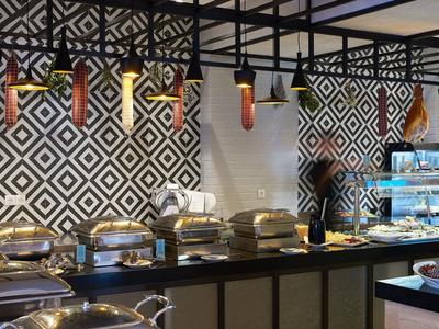 Buffet mit warmen Speisen in weißen Schalen, geometrische schwarz-weiße Wandgestaltung, moderne Lampen.