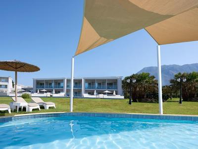 Pool mit klarem Wasser, Liegestühle und Sonnenschirme vor modernen weißen Gebäuden und Bergen.