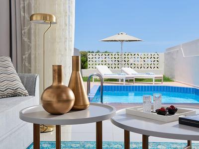 Balkon mit blauem Pool, zwei runden Tischen, goldenen Vasen und weißem Sofa vor blauem Himmel.