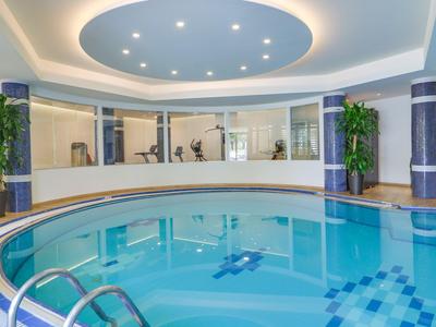 Indoor hotel pool with circular shape and modern ceiling lighting.