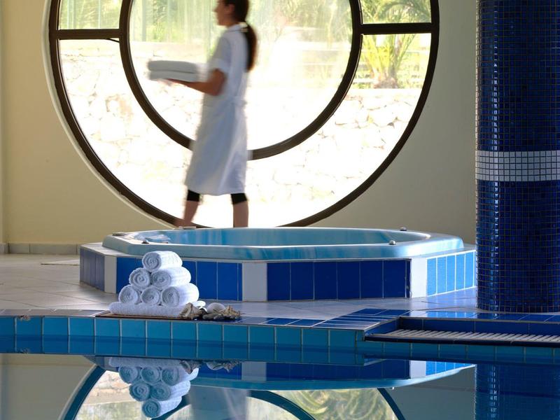 Woman in bathrobe walking by round window beside pool with pillar.