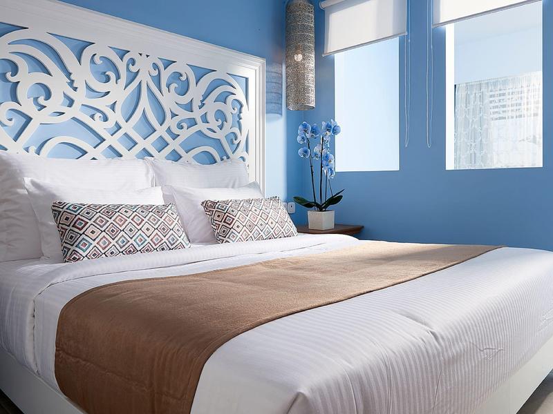 Modern bedroom with white ornate headboard, blue wall, and comfortable bed setup.