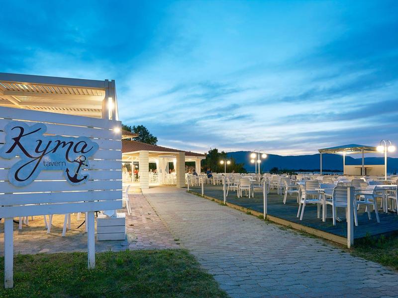 Evening view of an outdoor restaurant area with white chairs and tables under a blue sky.