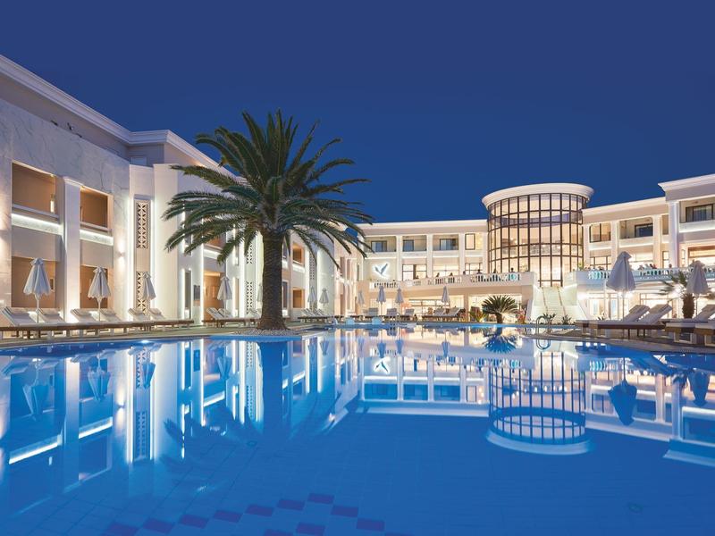 Luxury hotel with large pool and palm trees at dusk.