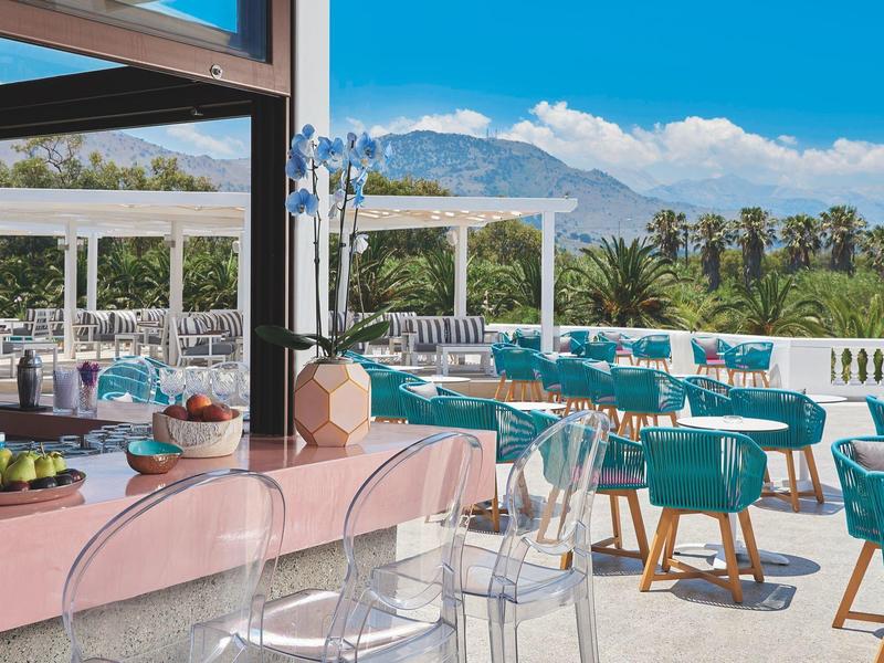 Modern hotel outdoor area with colorful chairs and mountain view on a sunny day.