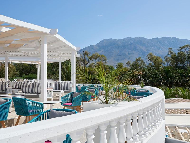 Outdoor lounge with turquoise chairs, pool, and mountain view under a blue sky.