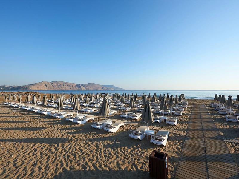 Empty loungers with folded umbrellas on a sandy beach under a clear sky.