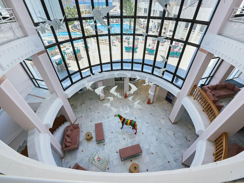 Top view of a bright hotel lobby with marble floor and glass windows overlooking the pool area.