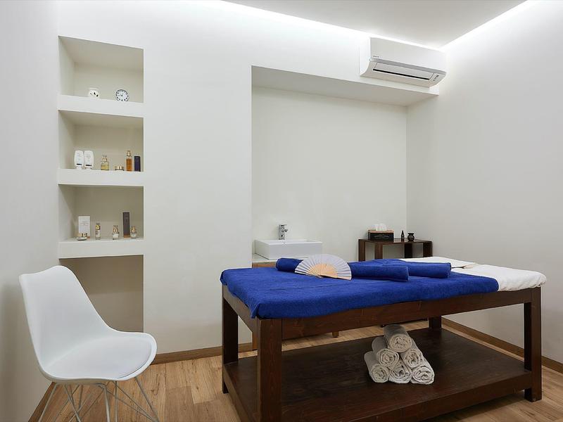 Simple treatment room with massage table, white chair, and modern air conditioner.