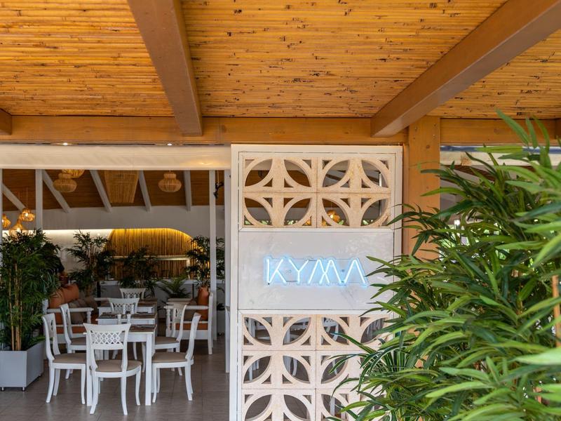 Modern hotel area with white chairs, green plants, and light blue neon sign on wall