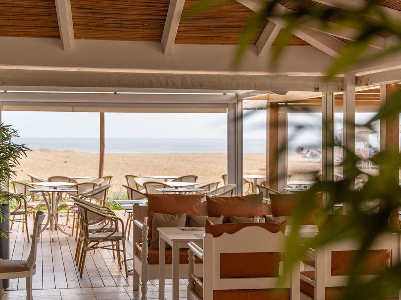 Bright restaurant with a view of the beach and sea through large windows.