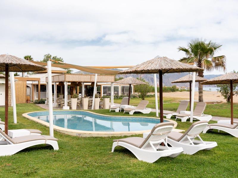 Pool area with sun loungers and umbrellas on a grassy lawn next to a building.