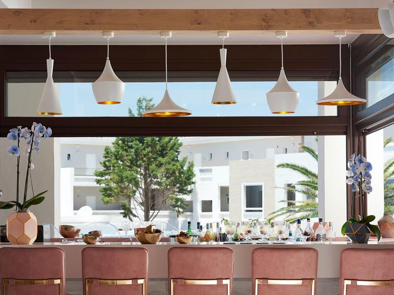 Modern hotel bar with pink stools, large windows, and decorative pendant lights.