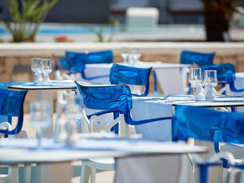 Empty patio chairs with blue covers and set tables outdoors in daylight