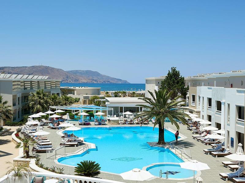 Hotel complex with multiple pools, palm trees, and sea view under clear sky.