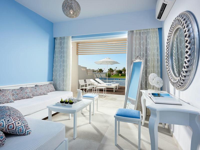 Bright hotel room with blue and white decor and balcony overlooking the sea.