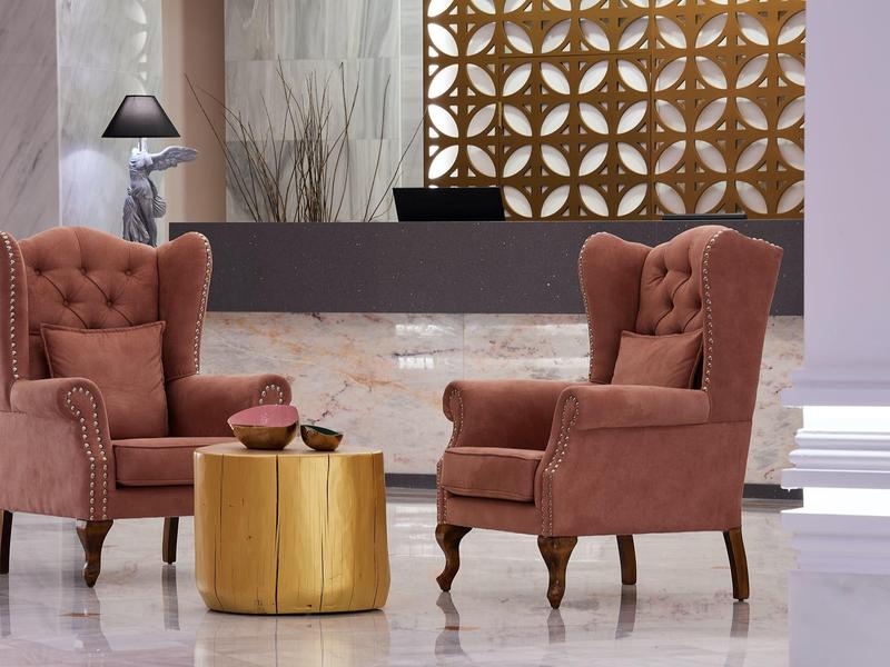 Elegant lobby area with two velvet armchairs and a round gold table in front of the reception.
