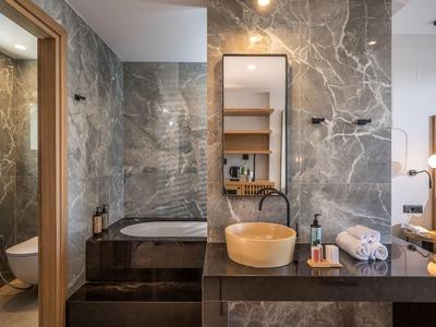 Baño moderno con azulejos de mármol, bañera incorporada y lavabo de madera.