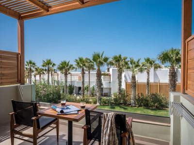 Balcón con sillas y mesa, vista de palmeras y cielo azul en un hotel.