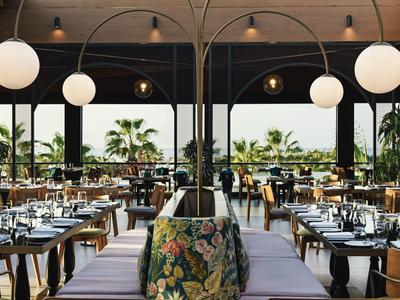 Offenes, modernes Restaurant mit Pflanzen, großem Blick und elegant gedeckten Tischen.