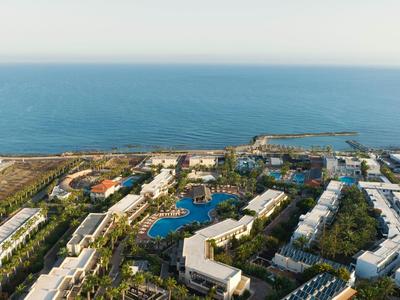 Luftaufnahme eines großen Hotels mit mehreren Pools an der Küste am Meer bei klarem Himmel.
