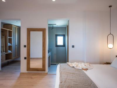 Dormitorio luminoso con cama grande, espejo de pared y baño abierto con ventana.