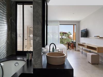 Baño moderno con bañera independiente y lavabo junto a una ventana con vista al salón.