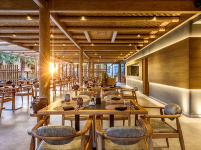 Nowoczesna część restauracyjna hotelu z drewnianymi stołami, krzesłami i ciepłym oświetleniem.