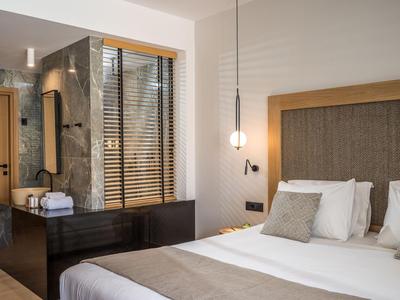 Nowoczesny pokój hotelowy z dużym łóżkiem, neutralnymi kolorami i oświetleniem pośrednim.