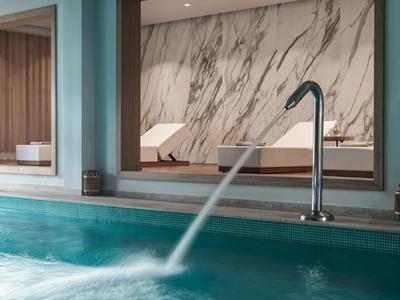 Nowoczesny basen kryty z funkcją wodospadu i marmurową ścianą w strefie spa hotelu.