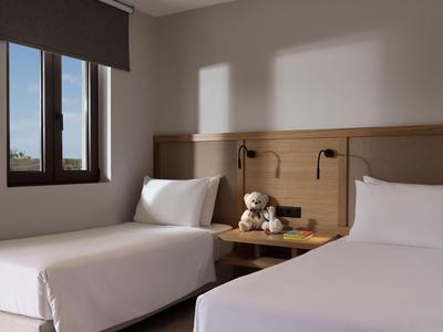 Pokój hotelowy z dwoma pojedynczymi łóżkami, białą pościelą i oknem z widokiem na zewnątrz.