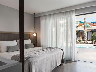 Nowoczesny pokój hotelowy z podwójnym łóżkiem i widokiem na basen przez przezroczyste zasłony.