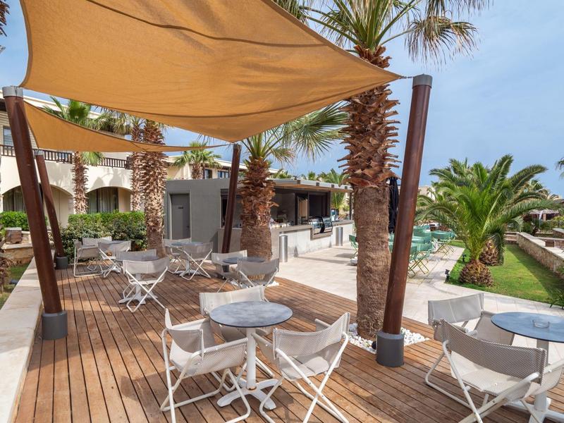 Sillas y mesas de salón al aire libre en una terraza de madera con toldo y palmeras