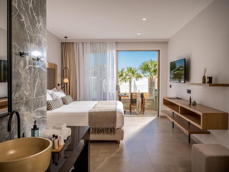 Habitación de hotel moderna con cama grande, balcón y vista a palmeras.