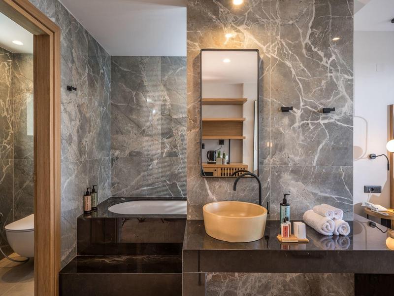 Baño moderno con azulejos de mármol, bañera incorporada y lavabo de madera.
