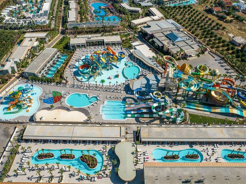 Vista aérea de un gran parque acuático con piscinas, toboganes y zonas de solarium en un resort vacacional.