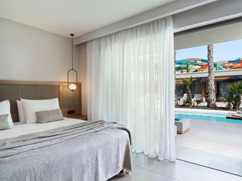 Habitación de hotel luminosa con cama grande, cortinas y vista a la piscina.