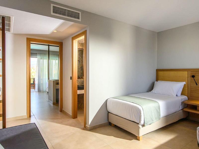 Una habitación de hotel luminosa con una cama individual, muebles de madera y acceso a baño y balcón.