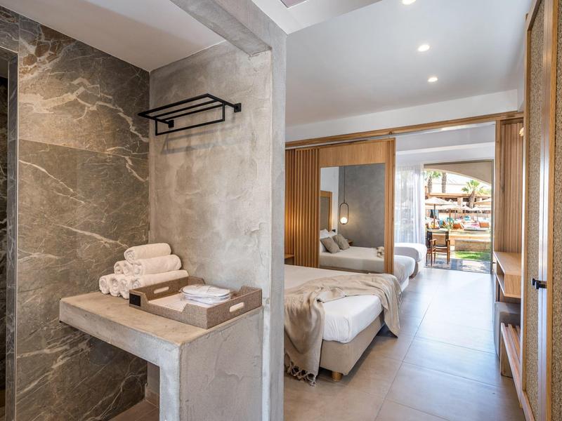 Habitación de hotel moderna con cama doble, baño con toallas y acceso a un balcón con área de estar.