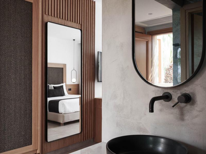 Habitación de hotel moderna con ropa de cama en blanco y negro, espejo y lavabo en primer plano.