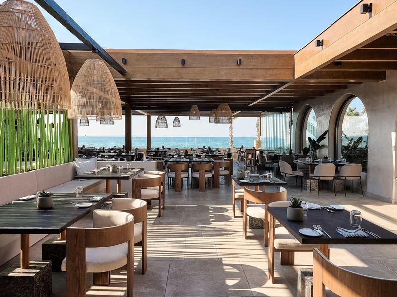 Restaurante abierto con muebles de madera y vista al mar en un día soleado.